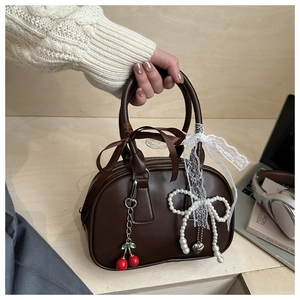 Detail of a brown leather pillow bag featuring cherry and pearl bow charm decorations