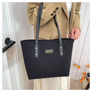 Detail view of black corduroy tote bag featuring a leather brand tag and golden rivets