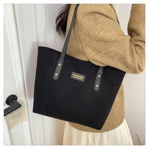 Detail of black corduroy tote bag with leather handles and gold rivet accents on shoulder