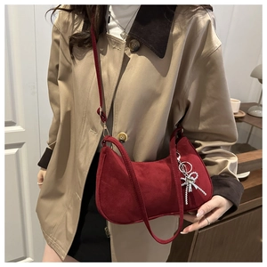 Detail of red suede crescent bag featuring a decorative silver bow tassel pendant