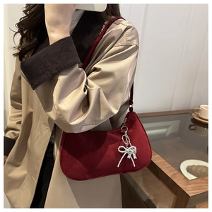 Detail of burgundy velvet shoulder bag with pearl bow charm worn by a model in a cafe