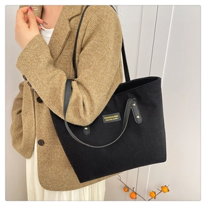 Detail of black corduroy tote bag with faux leather straps and golden rivet accents