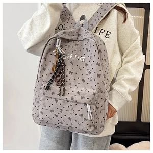 Detail eines grauen Cord-Rucksacks mit Schleifen-Print und Anhängern an einem Model