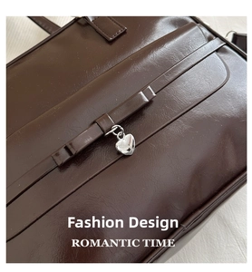 Detail of dark brown leather handbag featuring a polished silver heart-shaped metal pendant