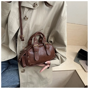 Detail of a vintage brown mini Boston bag with bronze buckles and rivets on textured leather