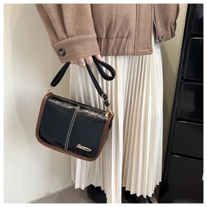 Close-up of black Boston bag with brown trim and gold logo worn by a model in a coat