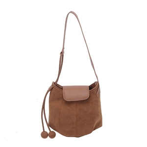 Brown faux suede minimalist bucket bag with decorative pompom tassels and adjustable strap