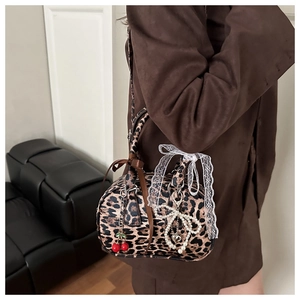 Detail of leopard print boston bag with cherry charms and lace bow on textured leather