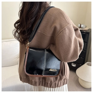Detail of black glossy shoulder bag with brown contrast edging and white stitching