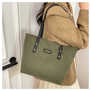 Close-up of military green corduroy tote bag featuring black leather handles and metal rivets
