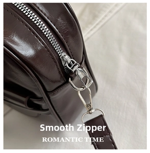 Detailed close-up of smooth silver metal zipper and hardware on dark brown leather bag