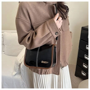 Detail of black glossy Boston bag with gold logo, contrast stitching, and brown edge paint