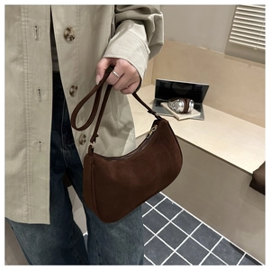 Close-up of a vintage brown matte baguette bag held in a modern office setting
