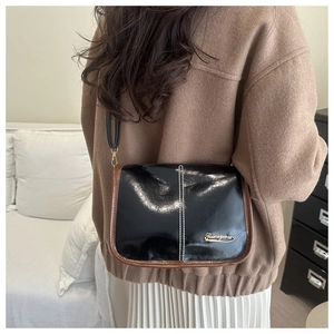 Detail of black patent leather shoulder bag with brown trim and gold logo emblem