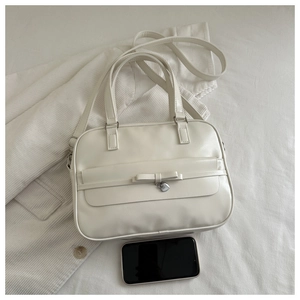 Close-up of beige faux leather handbag with bow detail and silver heart pendant charm