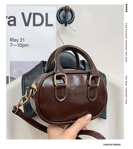 Detailed view of brown patent leather mini bowling bag with embossed logo and gold hardware