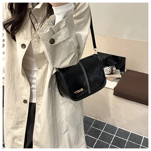 Detail of black glossy leather crossbody bag with white stitching and gold logo accent