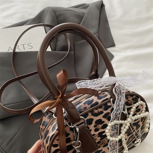 Leopard print cylinder handbag with pearl and lace charms on a grey blazer background