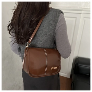 Close-up of brown glossy leather shoulder bag with white stitching and gold metal logo detail