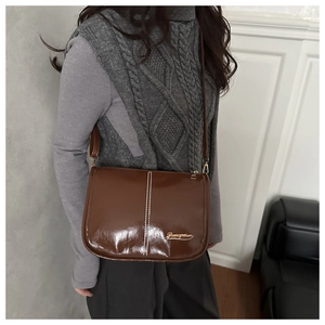 Detail of a brown oil-wax leather bag with white stitching and a golden logo plate