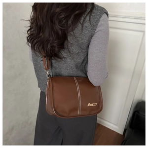 Detail view of a brown Boston bag with white stitching and gold logo on a model