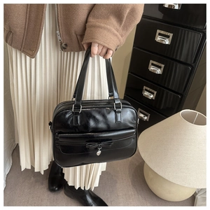 Detail of black PU leather handbag featuring a bow and heart pendant in a stylish setting