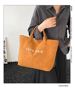 Model showing mustard yellow suede tote bag with white text in a minimalist setting