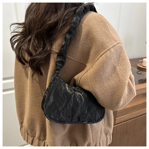 Detail of black pleated shoulder bag with silver bow buckle worn on model shoulder