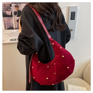 Detail of red velvet crescent bag with gold studs worn over a black coat