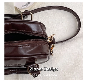 Detail view of the top gold zipper closure on the textured brown leather square bag