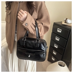 Close-up of black patent leather bag featuring a bow decoration and heart metal pendant