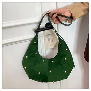 Detail of dark green suede hobo bag with golden stud rivets hanging on a handle