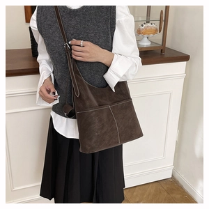 Detail of dark brown tote bag featuring contrast white stitching and front pocket design