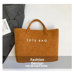 Flat lay of large brown suede tote bag with grey blazer and art book as styling props