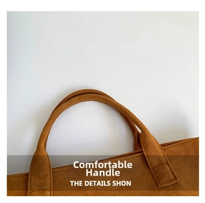 Detail of reinforced handles on a brown suede tote bag with precise stitching and soft texture
