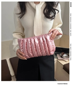 Detail der rosa Metallic-Clutch mit Falten-Design, getragen von einem Modell im Alltag