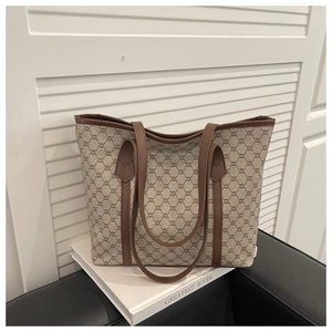 Close-up of monogram pattern tote bag with brown leather handles on white book props