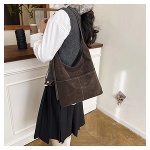 Detail of dark brown suede tote bag with contrast white stitching on a shoulder strap