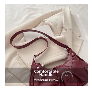Detail of burgundy Y2K biker bag with silver buckles and studs on a white blazer