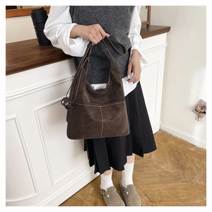 Detail of dark brown suede tote bag with contrast white stitching and round pendant