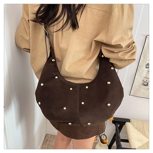 Detail of dark brown suede hobo bag with gold rivets worn by a model in a retro setting