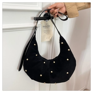 Dettaglio borsa hobo in camoscio nero con borchie dorate appesa a una porta bianca