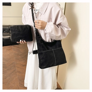 Model wearing a black contrast stitch hobo bag and matching pouch in a minimalist room