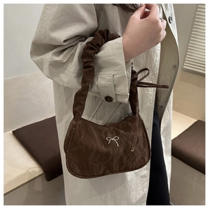 Detail of dark brown crescent bag with pleated handle and white bow accent on leather