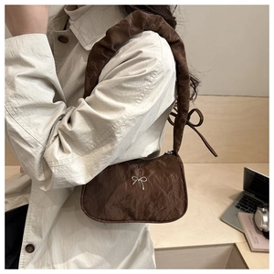 Detail of coffee brown pleated shoulder bag with silver bow and ruffled strap on desk