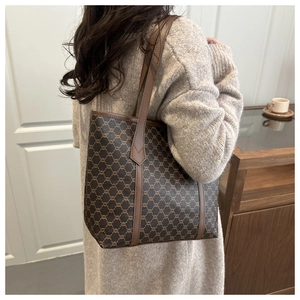 Brown monogram tote bag styled as a shoulder bag on a model in a warm interior setting