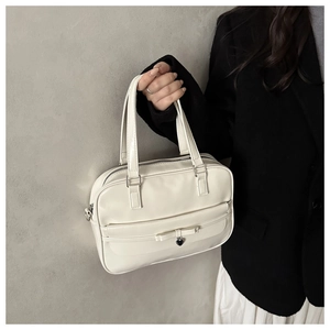 Detail of white leather pillow bag with bow and heart charm on a black coat