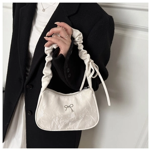 Close-up of a white pleated handbag featuring a silver metallic bow and soft ribbon detail