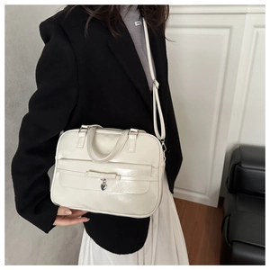 Detail of cream white glossy shoulder bag with bow and silver heart pendant on model