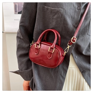 Close-up of a mini burgundy glossy leather bowling bag with gold hardware and logo texture